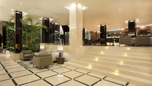 A hotel lobby with a checkered floor, a staircase, seating area with lamps, and a bar. - Madeira Turim Santa Maria Hotel (Funchal)