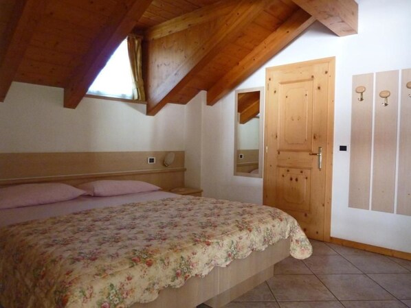 Un dormitorio con techo de madera, una cama con colcha floral, una puerta de madera y un espejo en la pared.