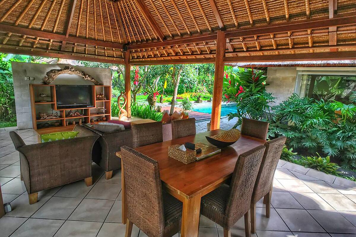 An outdoor patio with a wooden table and wicker chairs, a television, and a decorative shelf.