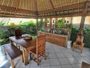 A wooden dining area with a table and chairs, a small kitchen with a sink and a toaster, and a thatched roof structure.