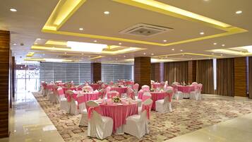 A banquet hall with round tables, white chairs, and pink decorations.