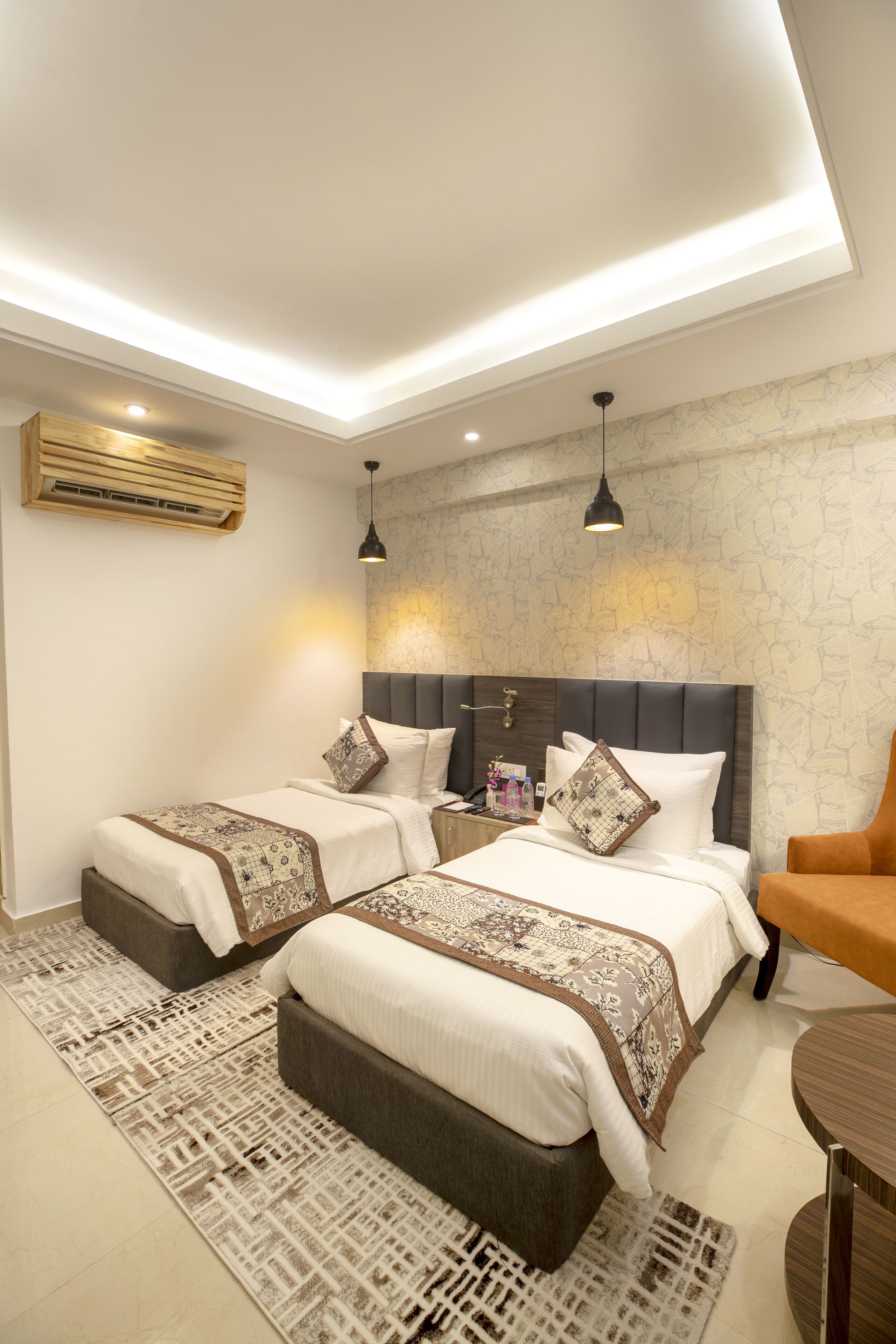 A modern bedroom with two beds, a sofa, a small table, and a patterned rug.