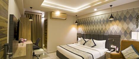 A modern hotel room with a large bed, a desk, a chair, and a sofa.