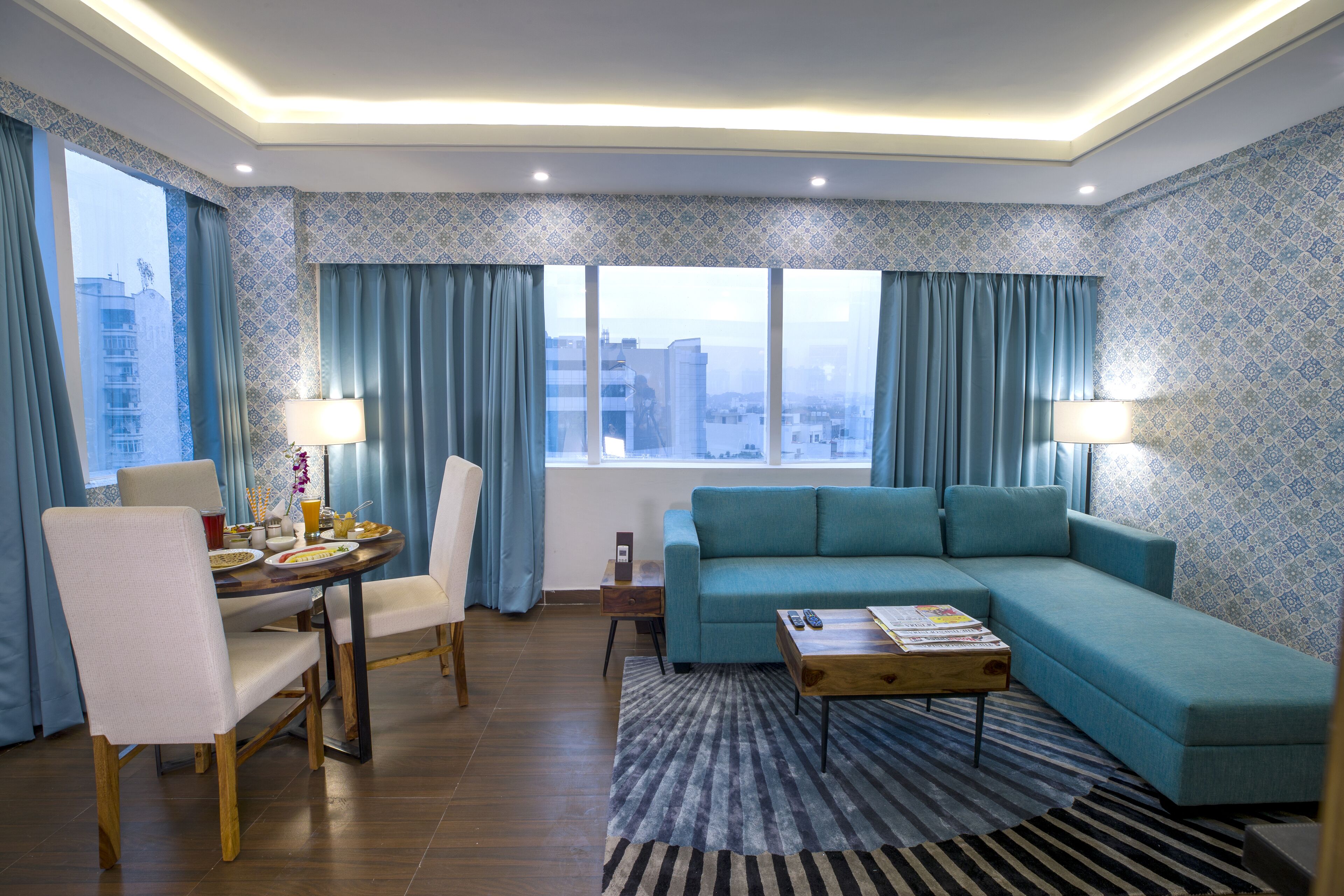A modern living room with a sofa, dining table, chairs, and a view of the city through large windows.