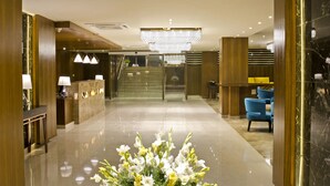 A hotel lobby with a reception desk, a chandelier, a floral arrangement, and a staircase. - Regenta Central Noida (Noida)