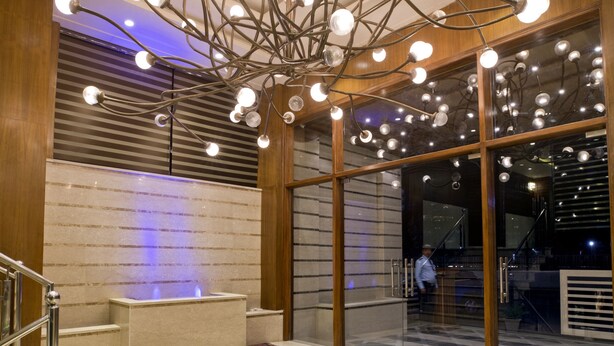 A modern lobby with a unique ceiling light fixture, a marble floor, and a staircase with metal railings. - Regenta Central Noida (Noida)