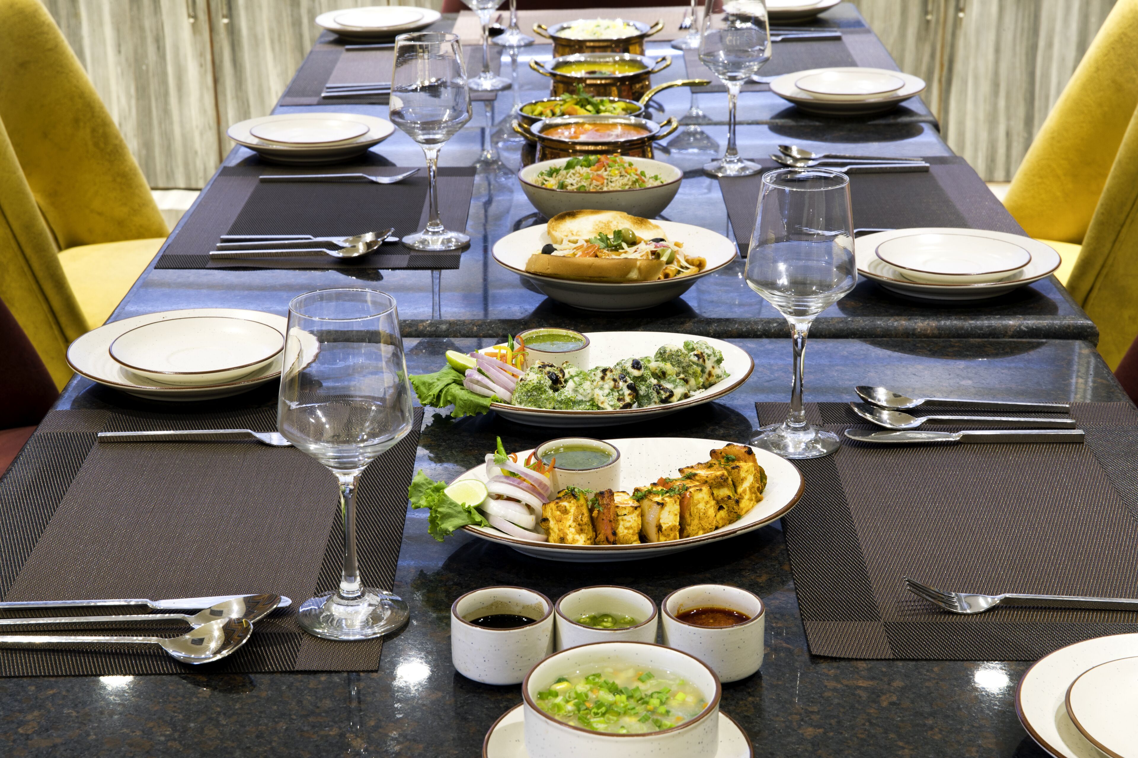 Une longue table à manger, dressée pour un repas copieux avec de nombreux plats, des verres et des couverts.