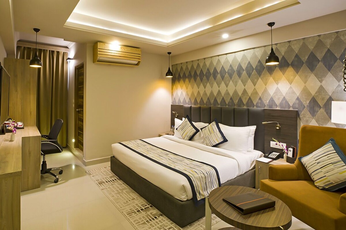 A modern hotel room with a large bed, a desk, a chair, and a small table.