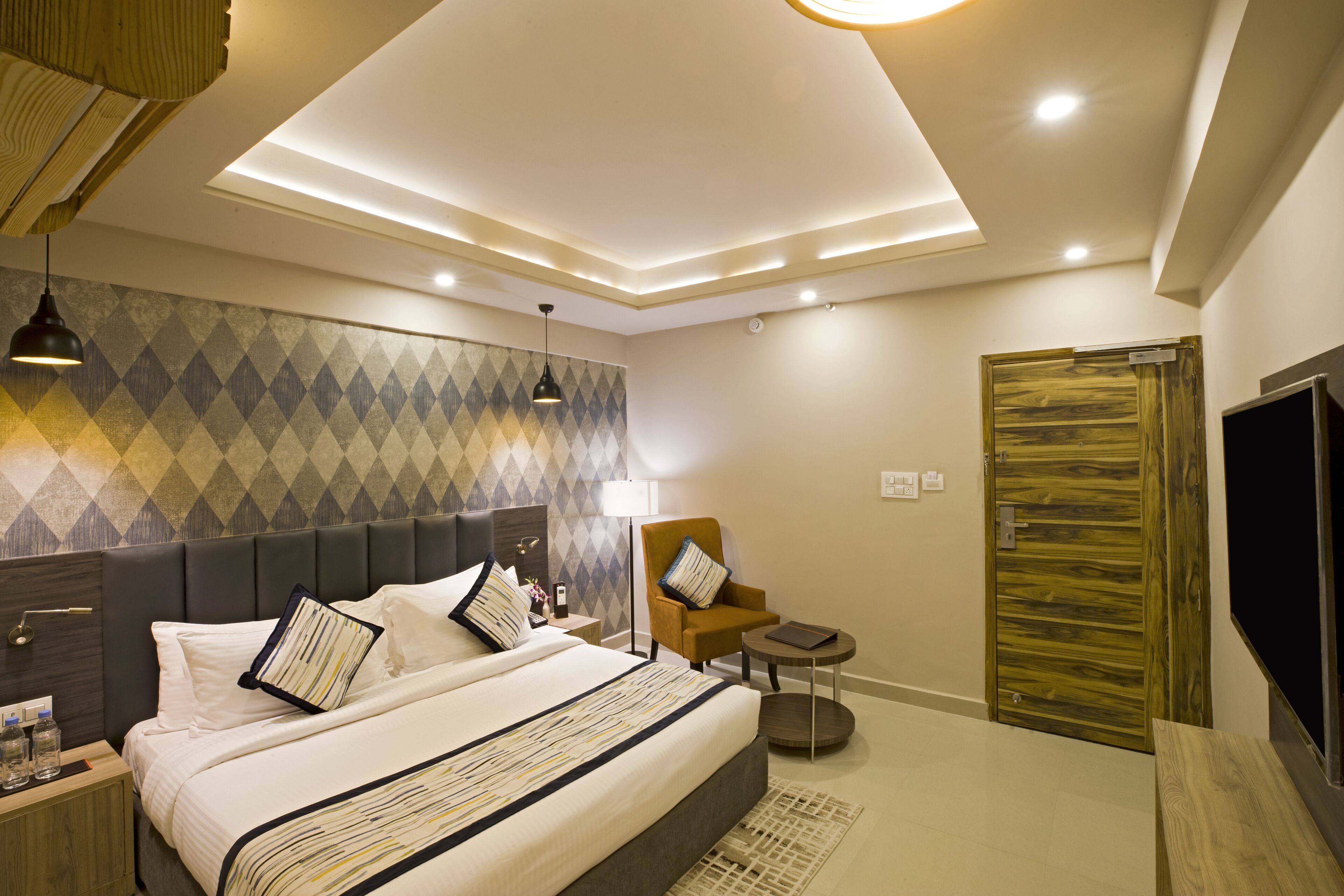 A modern hotel room with a large bed, a wooden door, a TV, and a small round table.