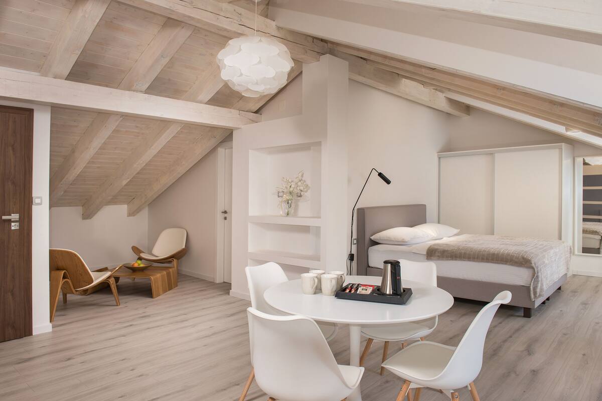 Ein modernes Schlafzimmer mit einer Schlafgalerie, einem Bett, einem Schreibtisch mit Stühlen und einer kleinen Sitzecke.