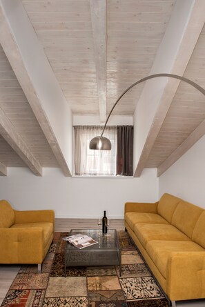 Ein Zimmer mit schrägen Wänden, zwei gelbe Sofas, einem Glastisch und einem gemusterten Teppich.