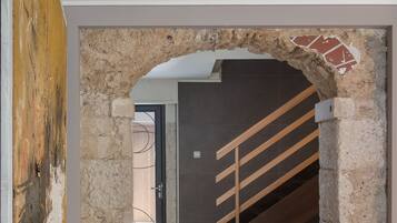 Un couloir orné d’une arche en pierre, d’un escalier et d’un grand tableau abstrait accroché au mur.