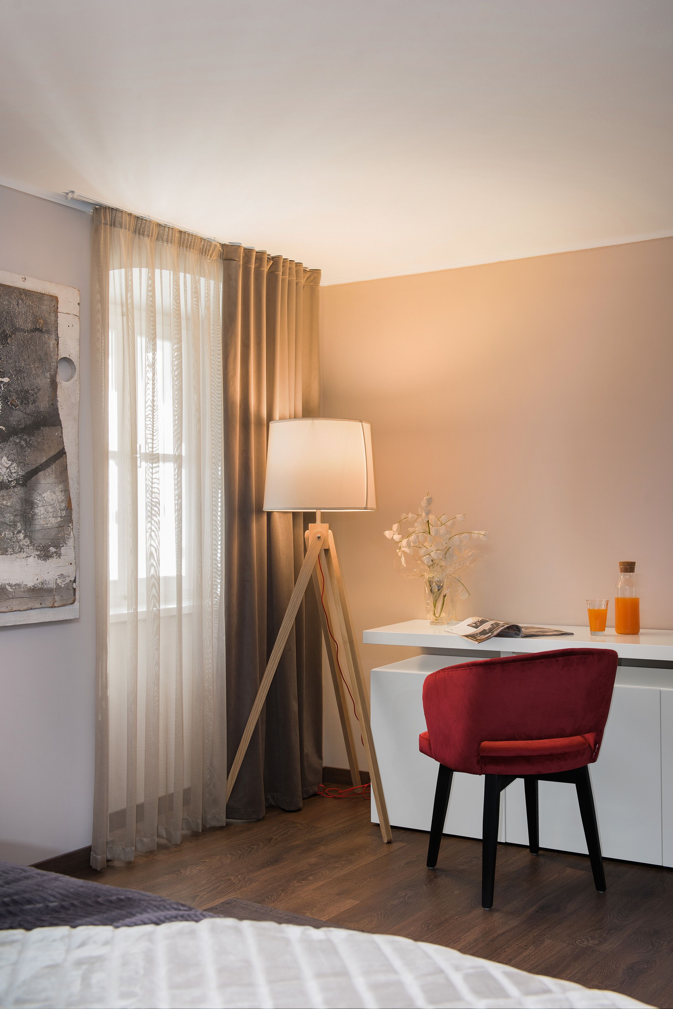 A hotel room with a bed, a desk with a lamp, a chair, and a window with curtains.