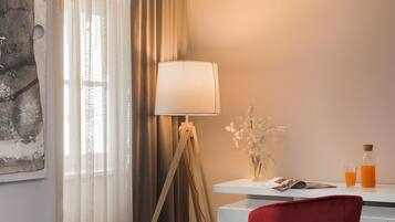 A hotel room with a bed, a desk with a lamp, a chair, and a window with curtains.