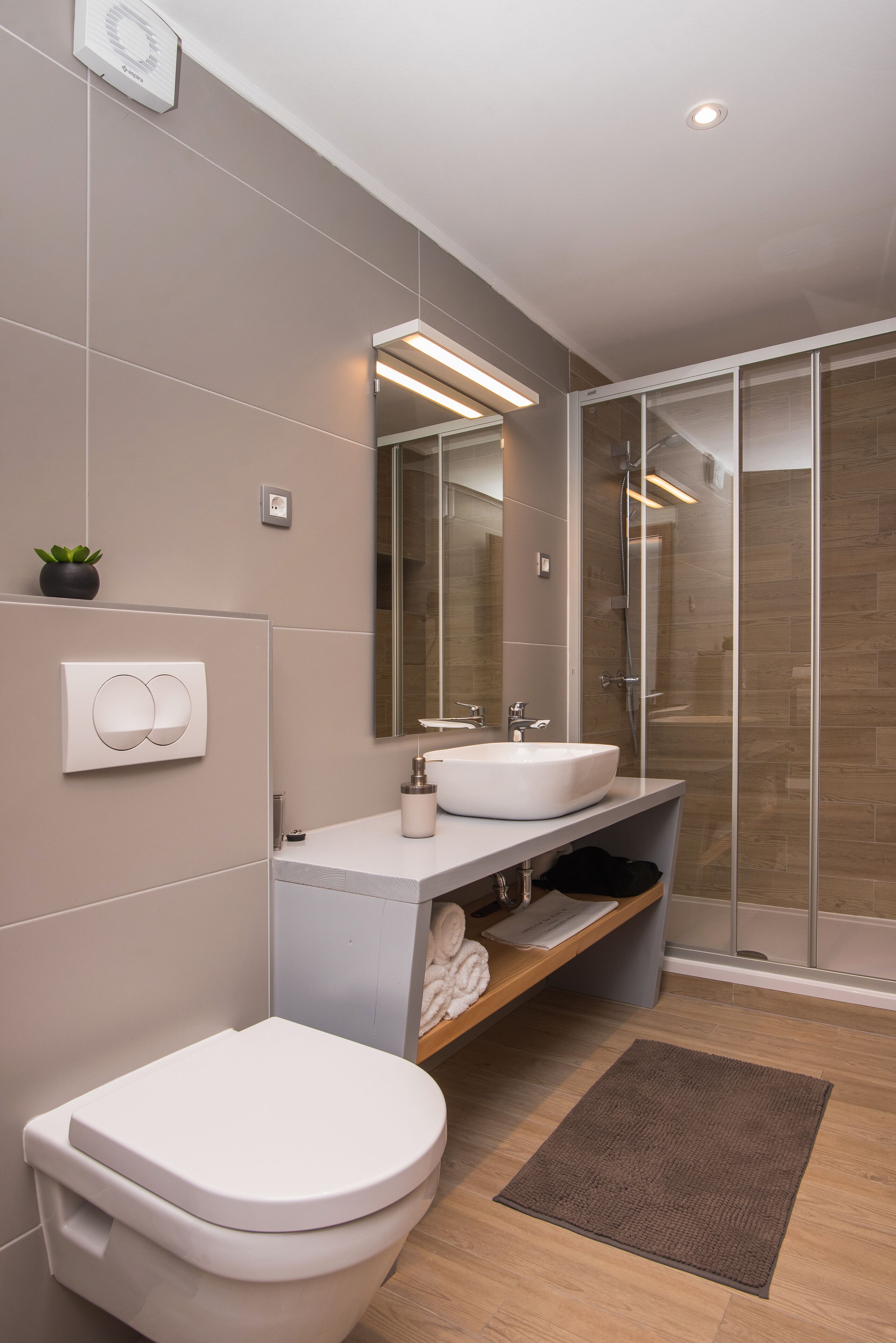 A modern bathroom with a toilet, two sinks, a shower, and a mirror.