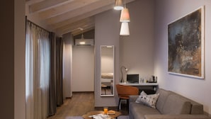 Une chambre d’hôtel moderne avec un plafond en bois, un canapé gris, une table basse en bois avec des magazines, un bureau avec un ordinateur portable et un grand tableau abstrait accroché au mur.