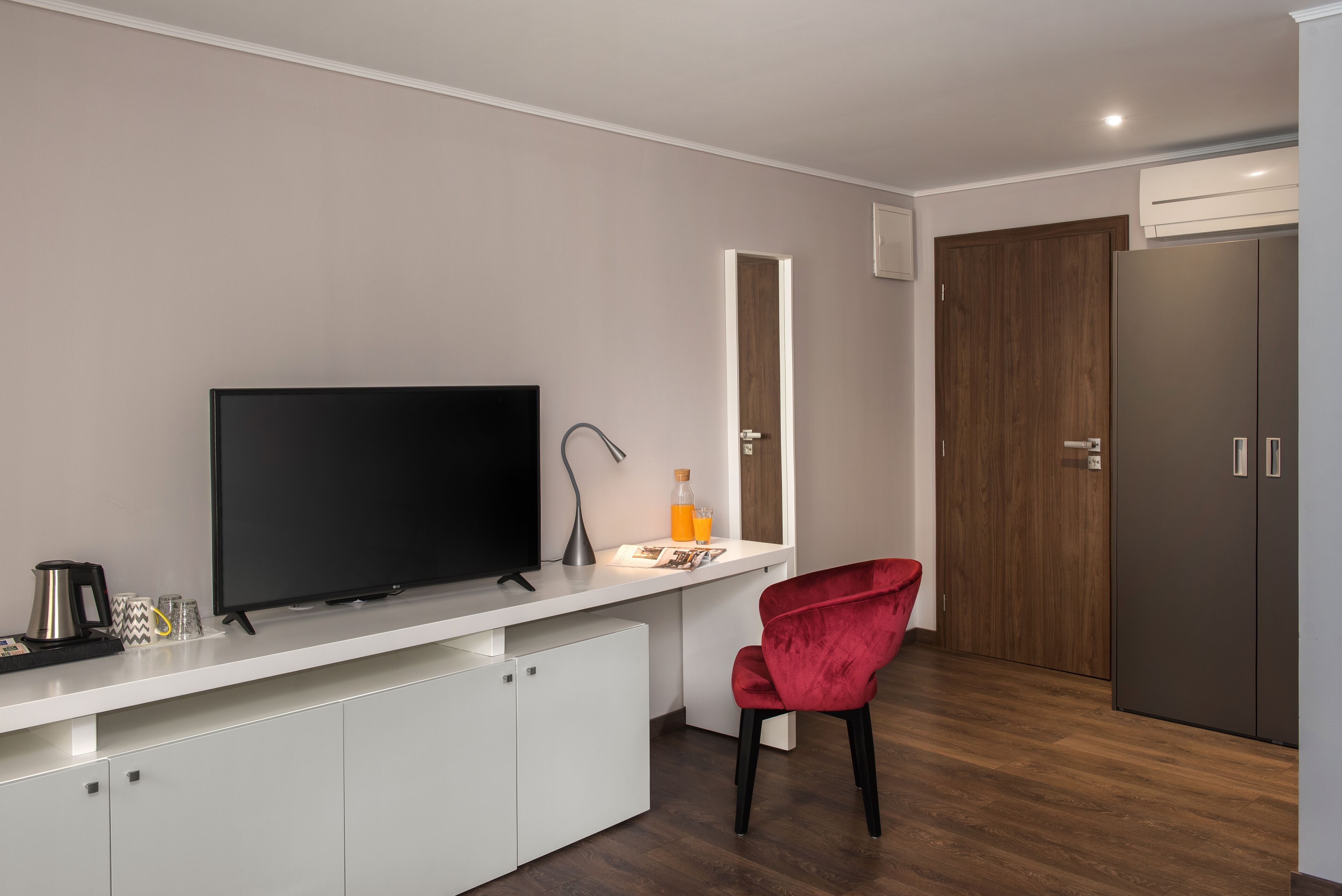 A modern kitchen with a flat-screen TV, a white countertop, a red chair, and a wooden door.