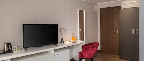 A modern kitchen with a flat-screen TV, a white countertop, a red chair, and a wooden door.