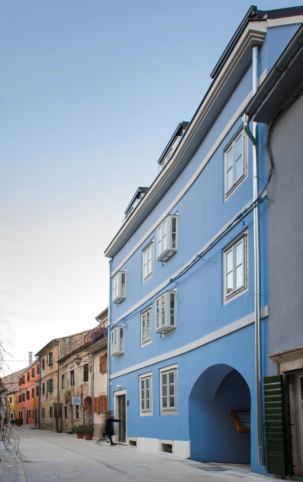 Straßenansicht eines blauen Gebäudes mit zahlreichen Fenstern und einem gut sichtbaren Eingang.
