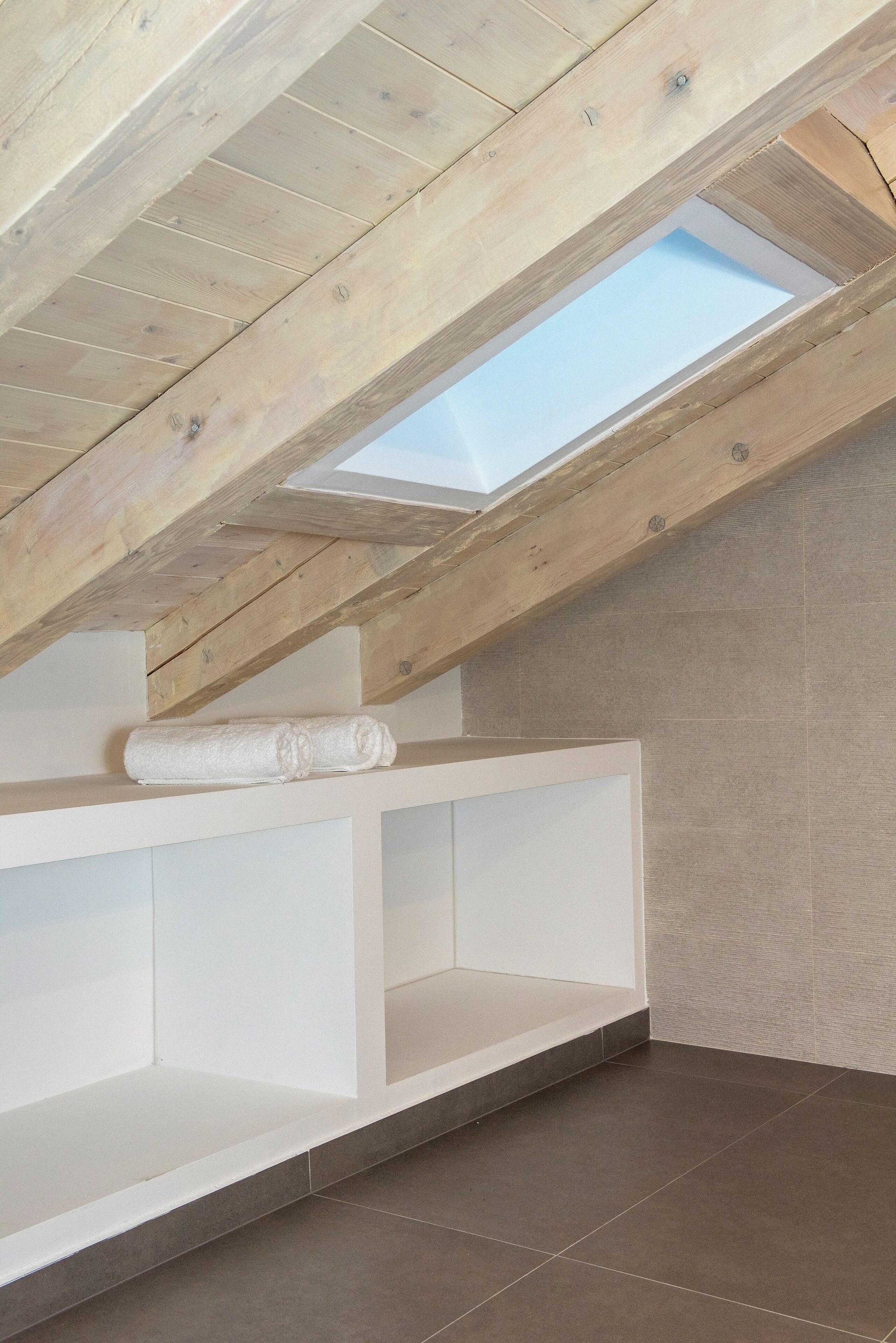 A modern bathroom with a skylight, white cabinetry, and a towel on the shelf.