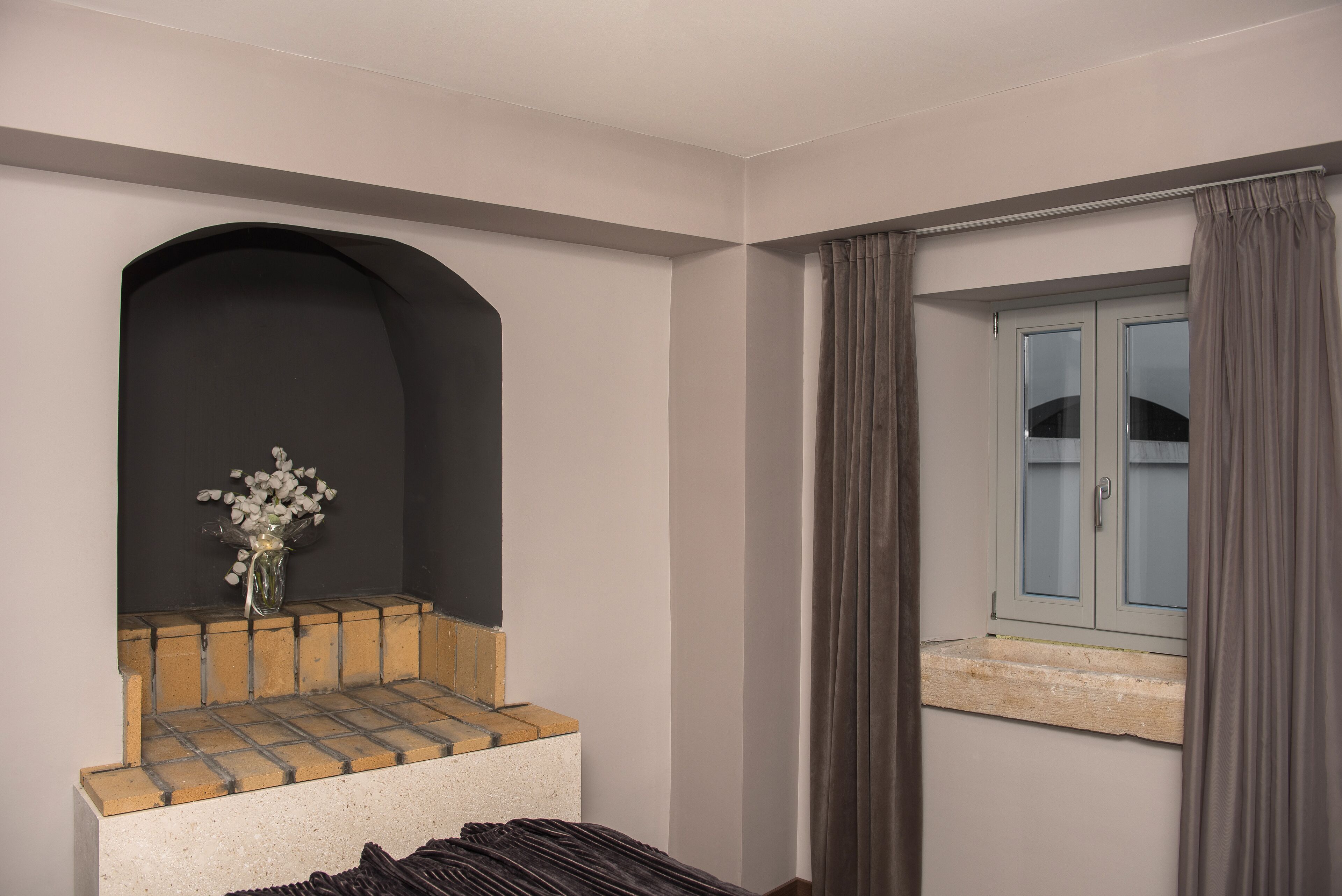 A room with a built-in bench, a small window with curtains, and a vase with flowers on a ledge.