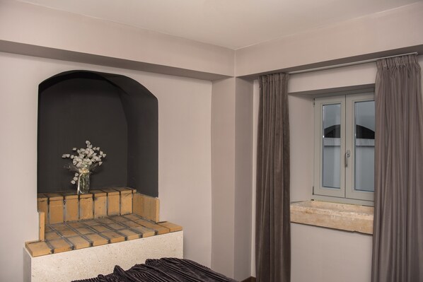 A room with a built-in bench, a small window with curtains, and a vase with flowers on a ledge.