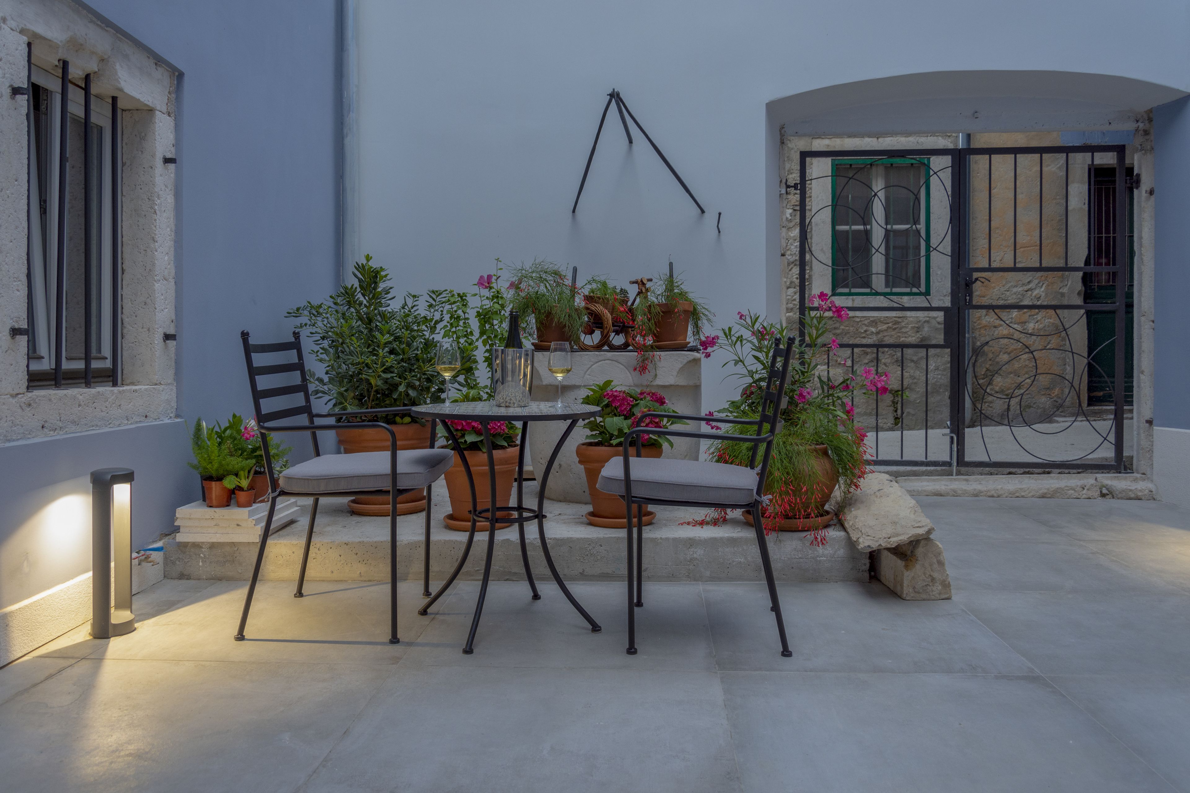 Una terrazza esterna con tavolo e sedie, circondata da vasi di piante e fiori.