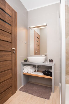 Ein modernes Badezimmer mit Holztür, weißem Waschbecken, Spiegel und Handtuchhalter.