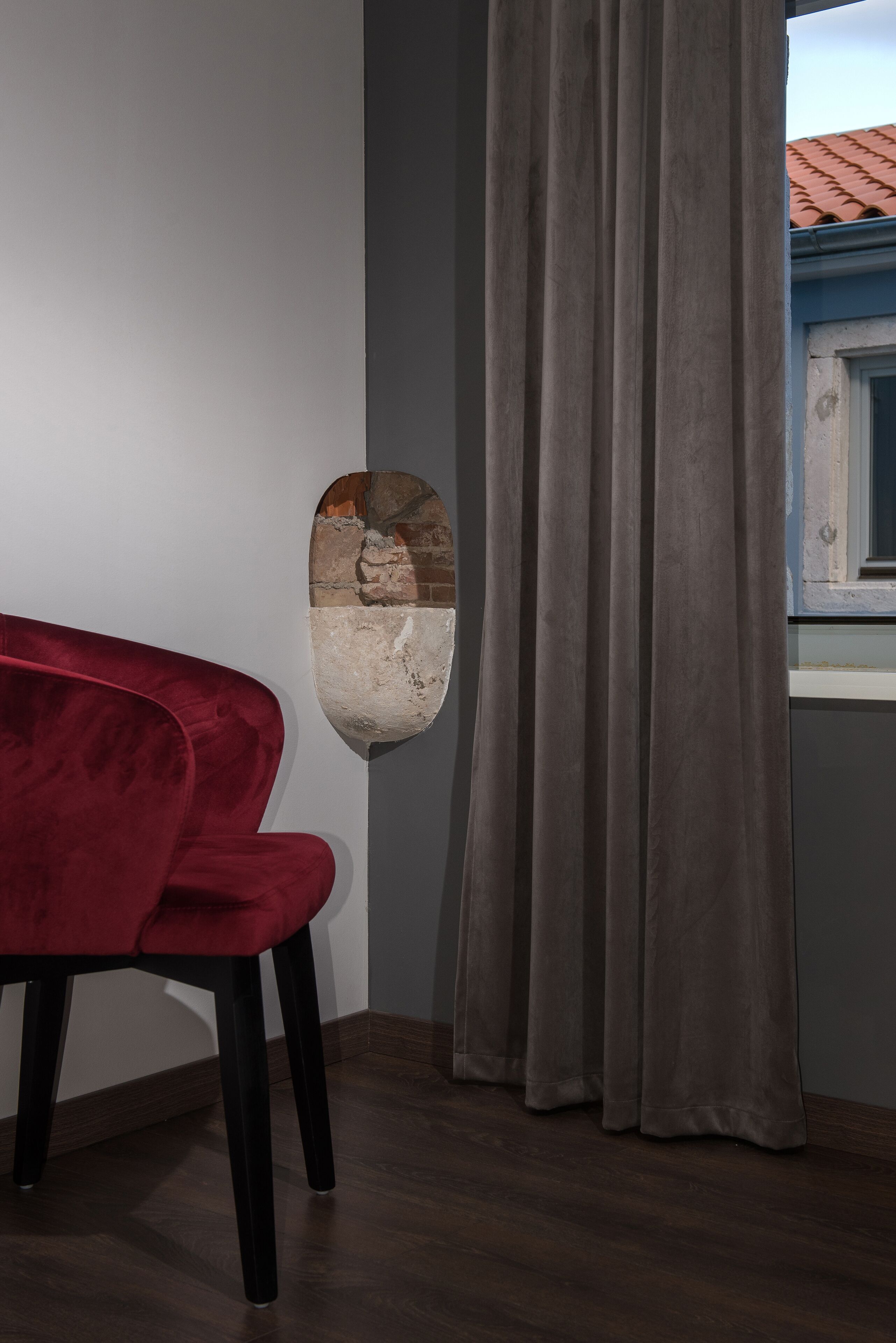 Una habitación con una silla roja, una cortina gris y un objeto sujeto a la pared.