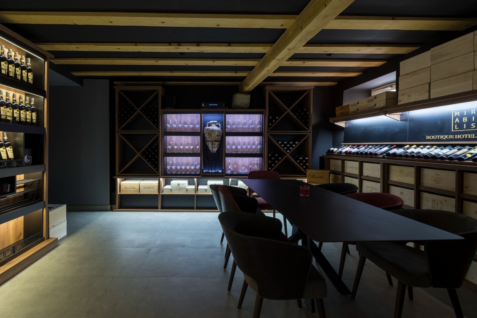 A modern bar area with wooden beams, wine racks, and a long table with chairs.