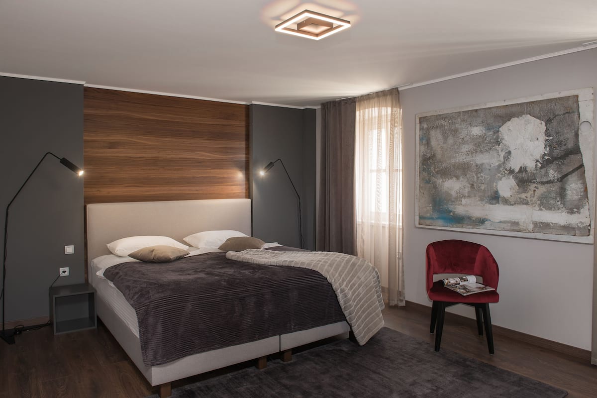 Ein modernes Schlafzimmer mit einem Bett, Nachttischlampen, einem roten Sessel und einem großen abstrakten Gemälde an der Wand.