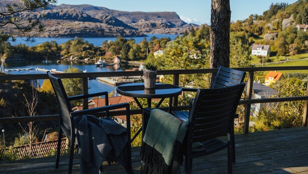 En terrass med ett bord och två stolar, med utsikt över en sjö och kullar.