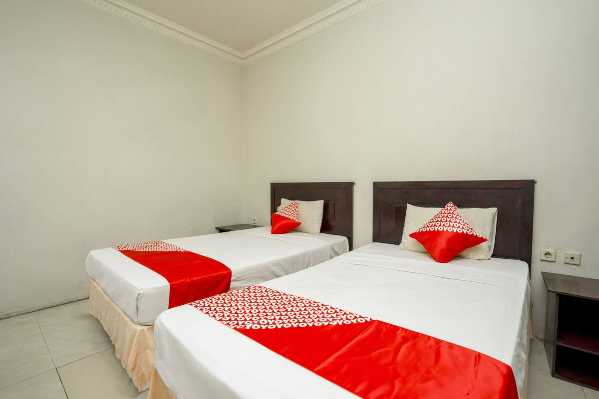 Two single beds with white and red bedding, a wooden headboard, and a white wall.