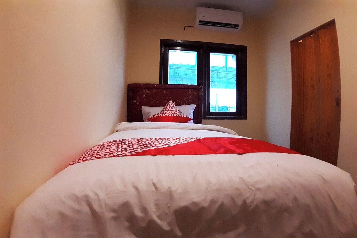 A narrow room with a bed, a window, and an air conditioning unit.