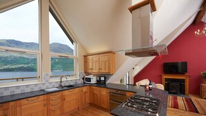 A modern kitchen with wooden cabinets, a granite countertop, a gas stove, and a view of a lake through large windows.