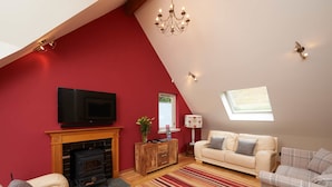 A cozy living room with a fireplace, a television, a sofa, and a window with natural light.