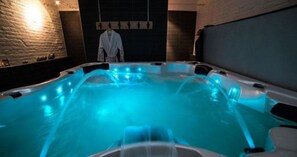 Un jacuzzi con iluminación azul, una bata colgada en un perchero y una pared de ladrillo.