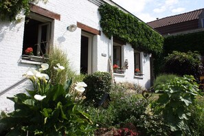 Een wit gebouw met meerdere ramen, waarvan sommige beplant zijn. Er ligt een tuin met verschillende planten en bloemen aan de voorzijde.