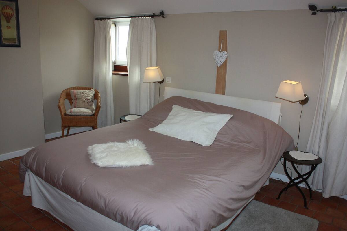 A bedroom with a large bed, two bedside tables, a chair, and a wall-mounted heart decoration.