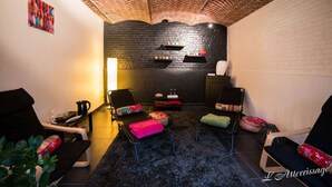 A cozy room with a brick wall, a black sofa, a small table, and a floor lamp. - L'Atterrissage (Santes)