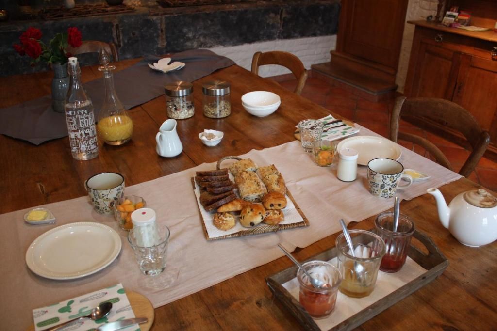 Une table de salle à manger en bois, sur laquelle sont disposés divers aliments pour le petit-déjeuner, notamment des viennoiseries et du pain, ainsi qu’un plateau contenant des condiments.
