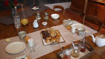 Une table de salle à manger en bois, sur laquelle sont disposés divers aliments pour le petit-déjeuner, notamment des viennoiseries et du pain, ainsi qu’un plateau contenant des condiments.