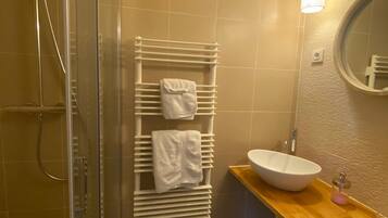 A bathroom with a glass shower enclosure, a white towel rack with towels, a round mirror, and a wooden countertop with a sink.