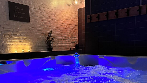 A spa area with a hot tub illuminated by blue lights, a brick wall, and a sign with text. - L'Atterrissage (Santes)