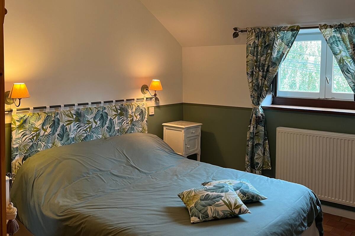 A bedroom with a bed, two bedside lamps, a nightstand, a radiator, and a window with curtains.