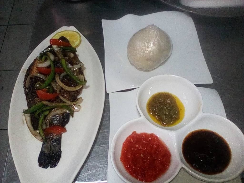 Un plato con pescado a la parrilla, verduras y una guarnición de pan y salsas.