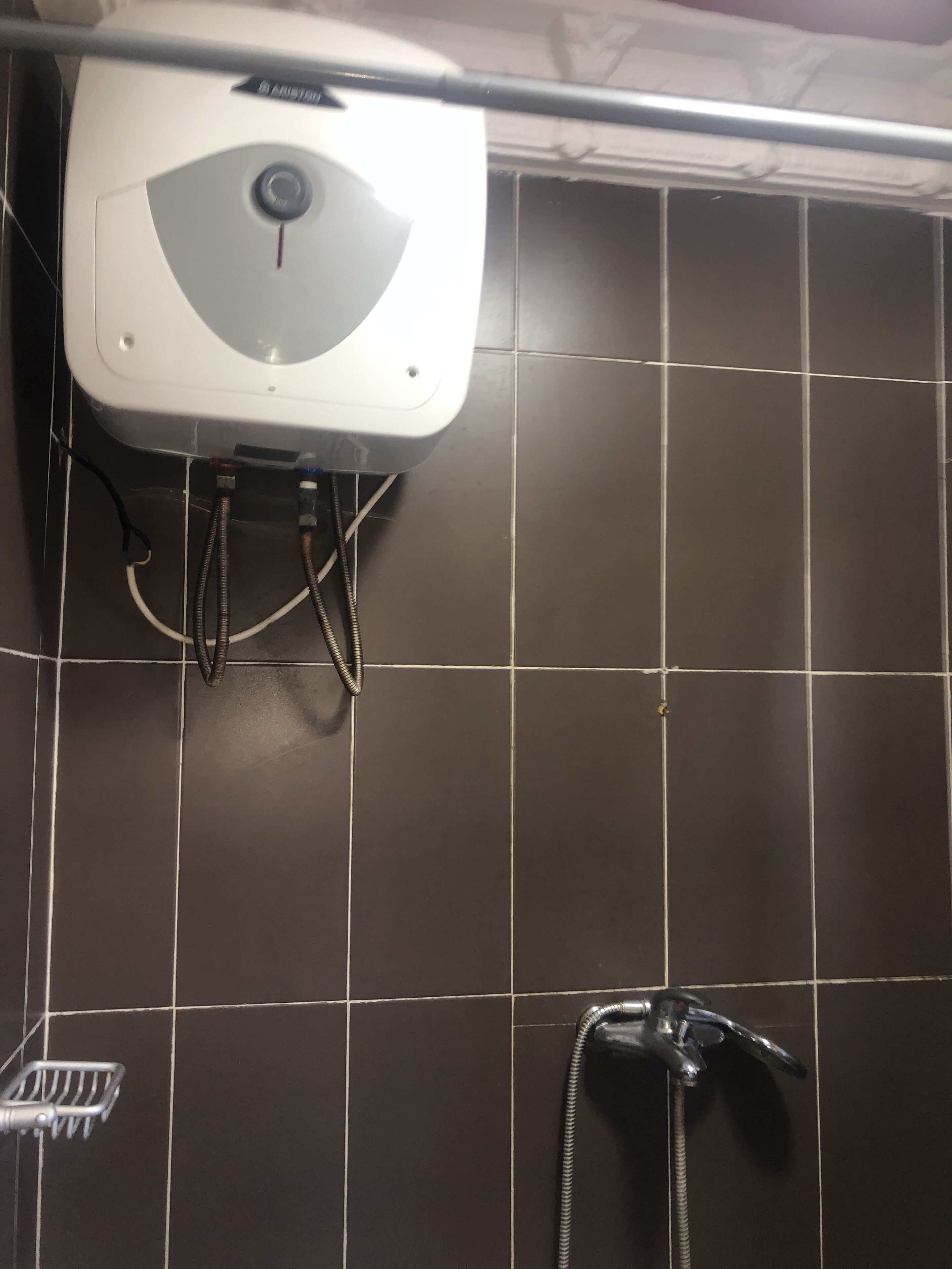 Un baño con un secamanos blanco montado en la pared, un cabezal de ducha y una bandeja de ducha de metal.