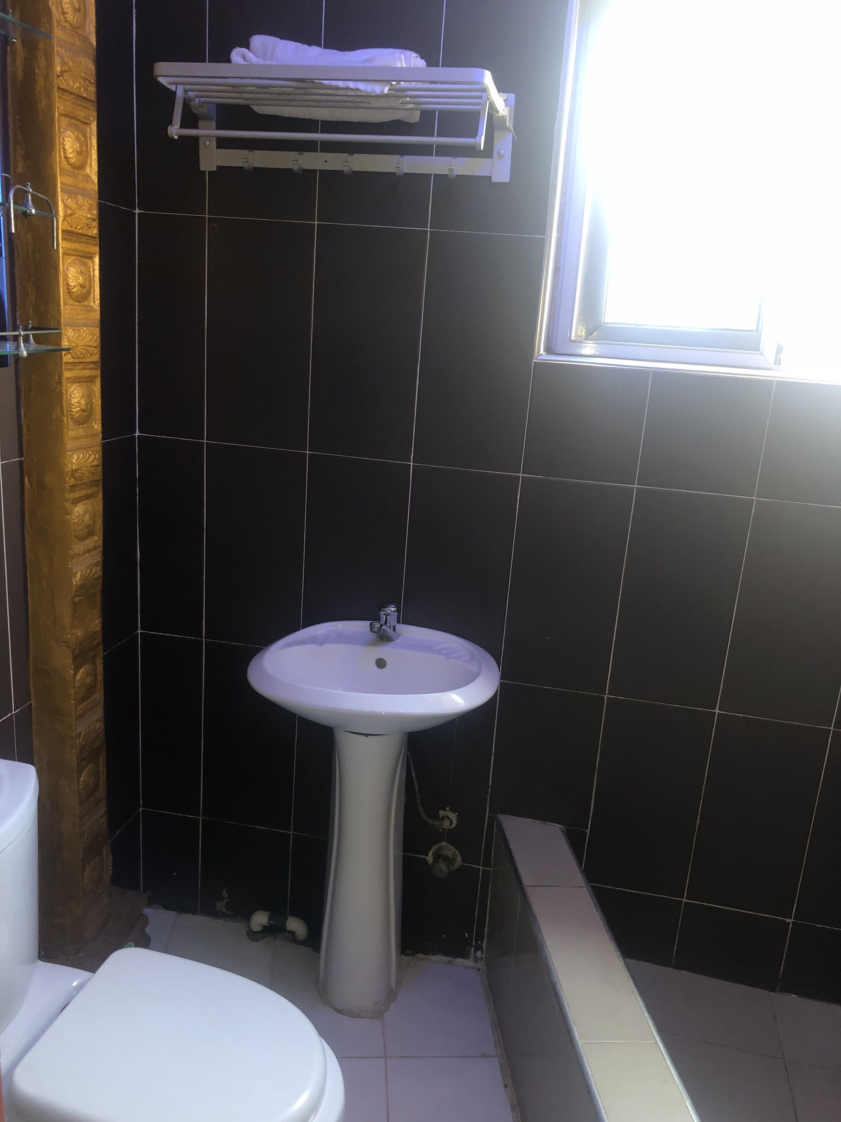 Un bagno con un lavandino bianco, un water e una vasca da bagno. Una finestra permette l'ingresso di luce naturale.