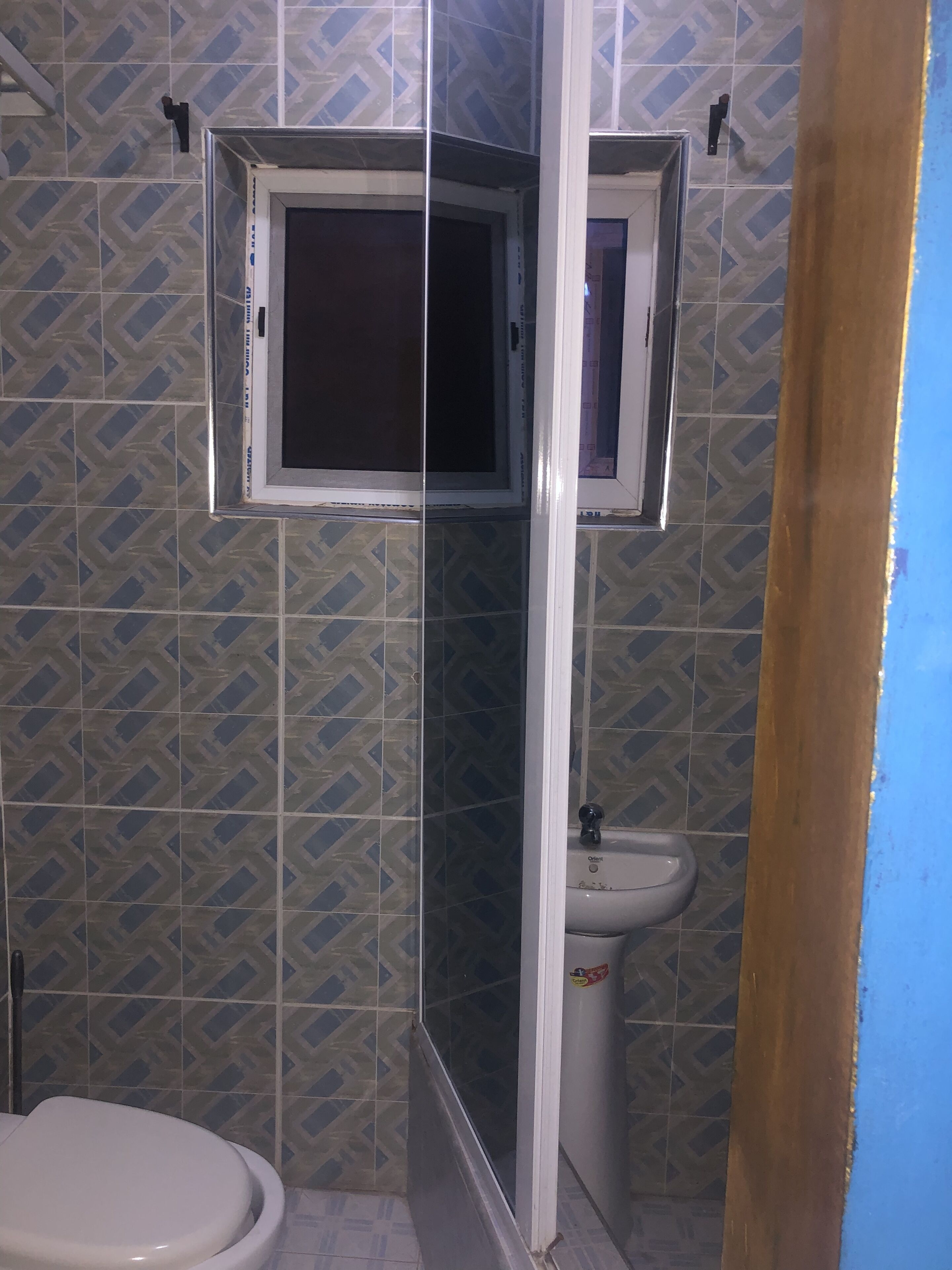 A bathroom with a tiled wall, a window, a sink, and a toilet.