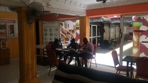 Restaurante com área de refeições, mesas, cadeiras, um ventilador e um painel de vidro.
